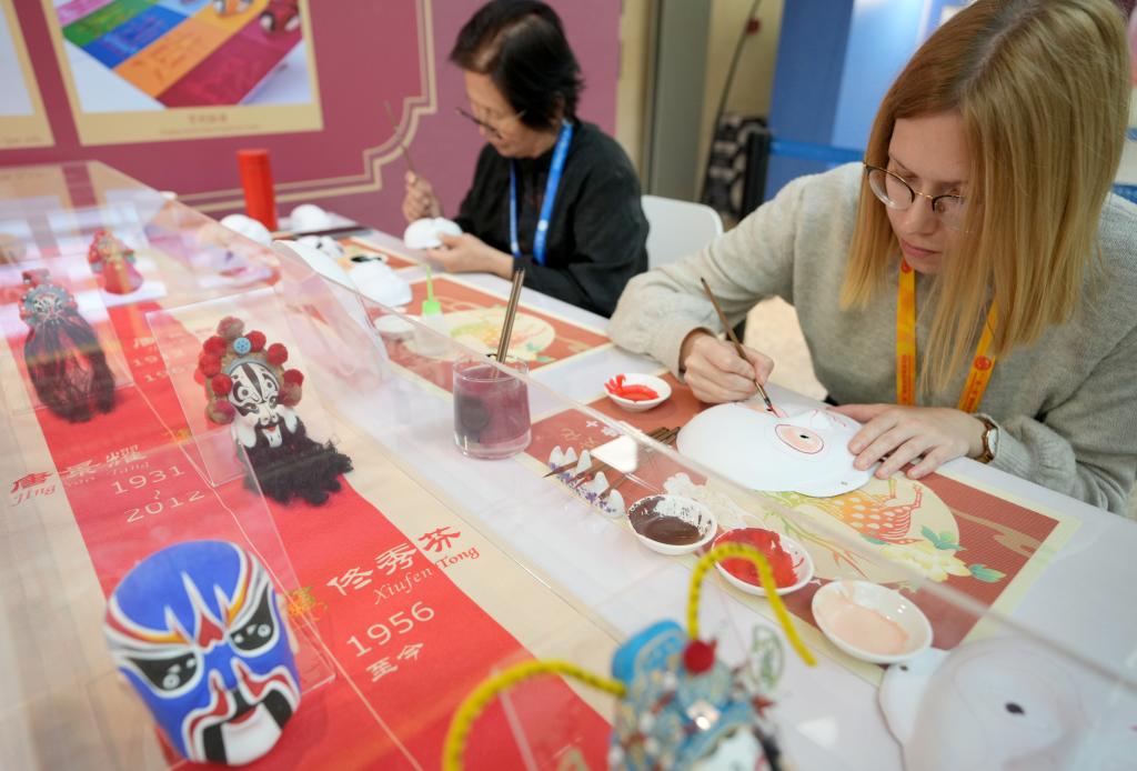 10月16日，在第三屆“一帶一路”國際合作高峰論壇新聞中心，來自比利時(shí)的記者（右）體驗(yàn)畫京劇臉譜。新華社記者 王毓國 攝