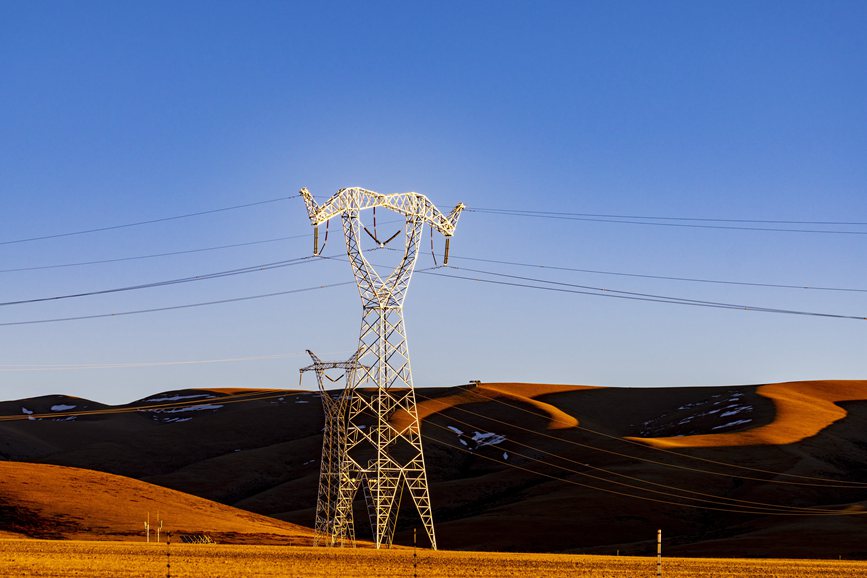 阿里地區(qū)的曠野上，電力鐵塔在夕陽下熠熠生輝。